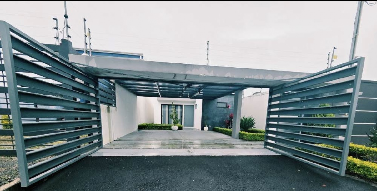 Cochera techada con piso de concreto y portón metálico gris abierto — casa en-venta en Santo Domingo
